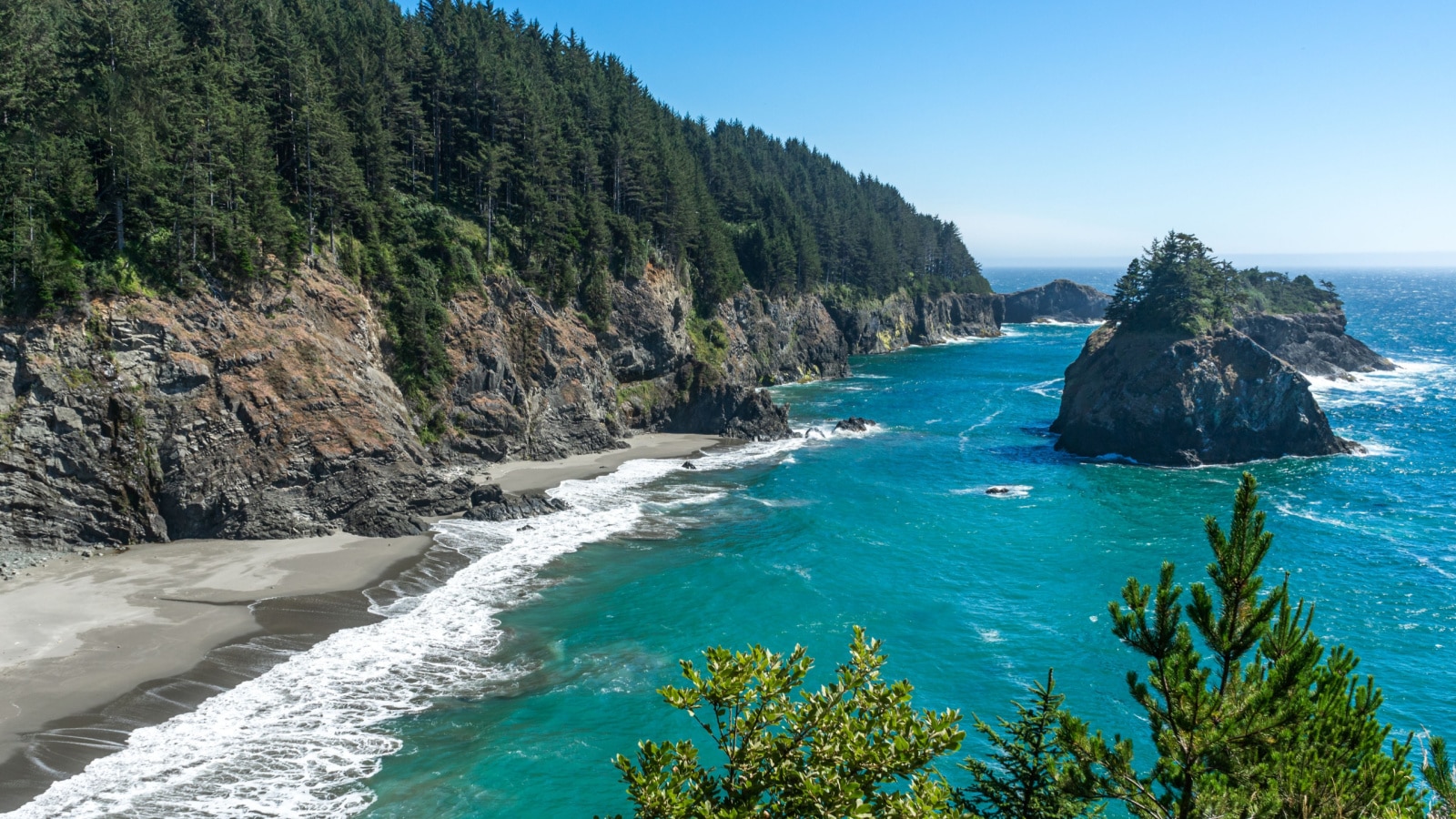A sunny afternoon image of the beach and rocky cliffs that are south of the Arch Rock in the southern part of the Oregon Coast.