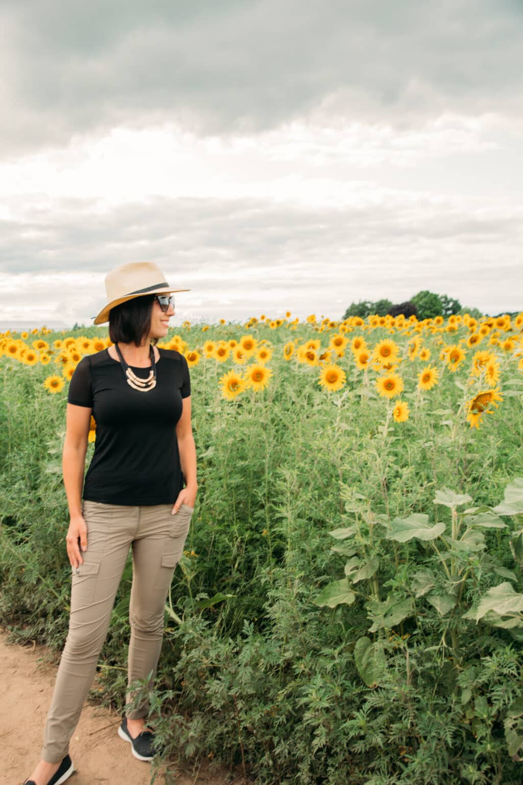 Wearing a black Anatomie t shirt with mesh sleeves and khaki skinny pants looking out at a field of sunflowers