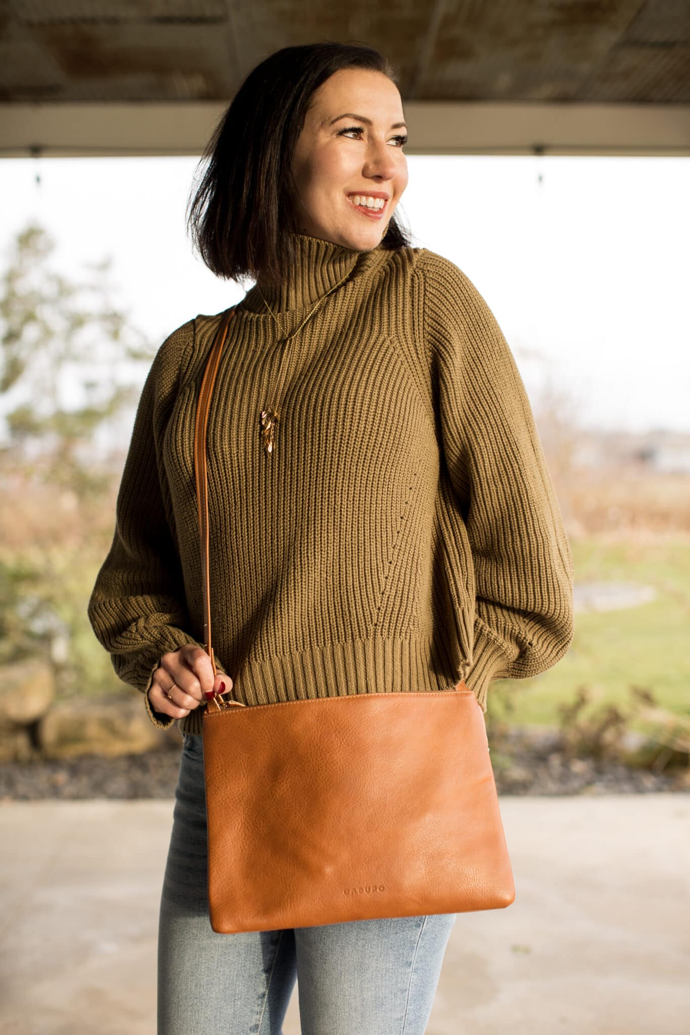 Lindsey wearing an olive green turtle neck sweater and jeans with a Casupo leather crossbody bag