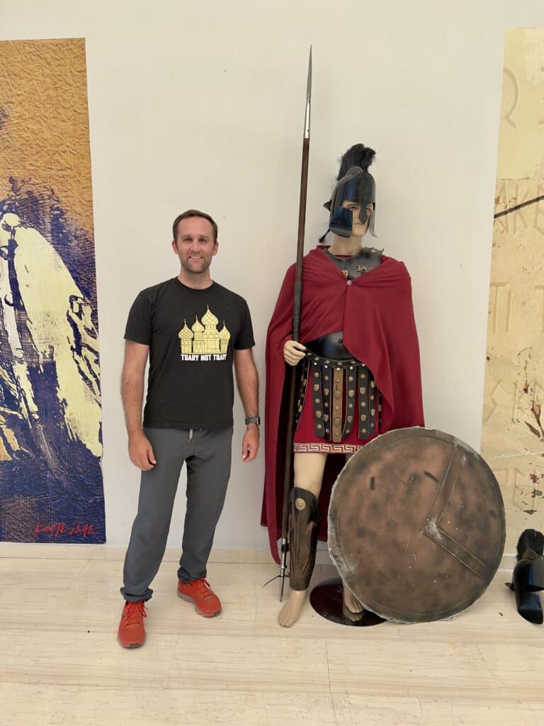 Zac wearing a t shirt and grey free fly pants standing next to a Spartan statue