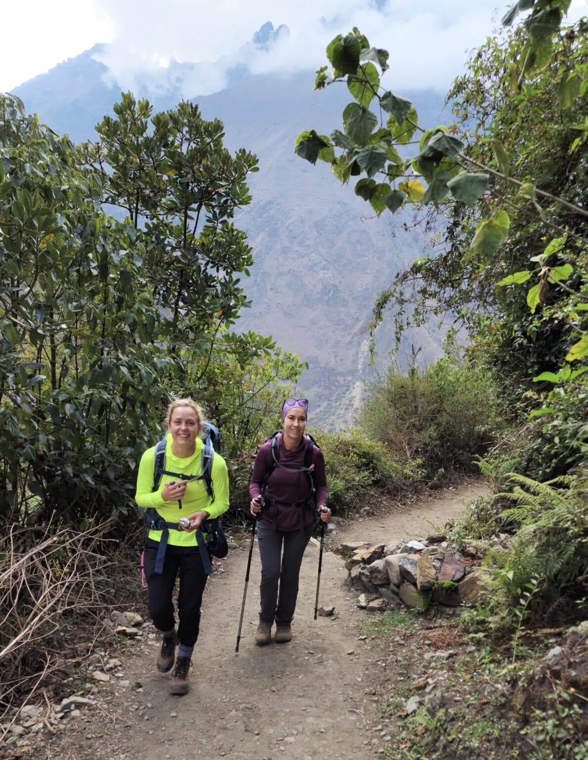 Two women hiking a trail in Peru with misty mountains in the background