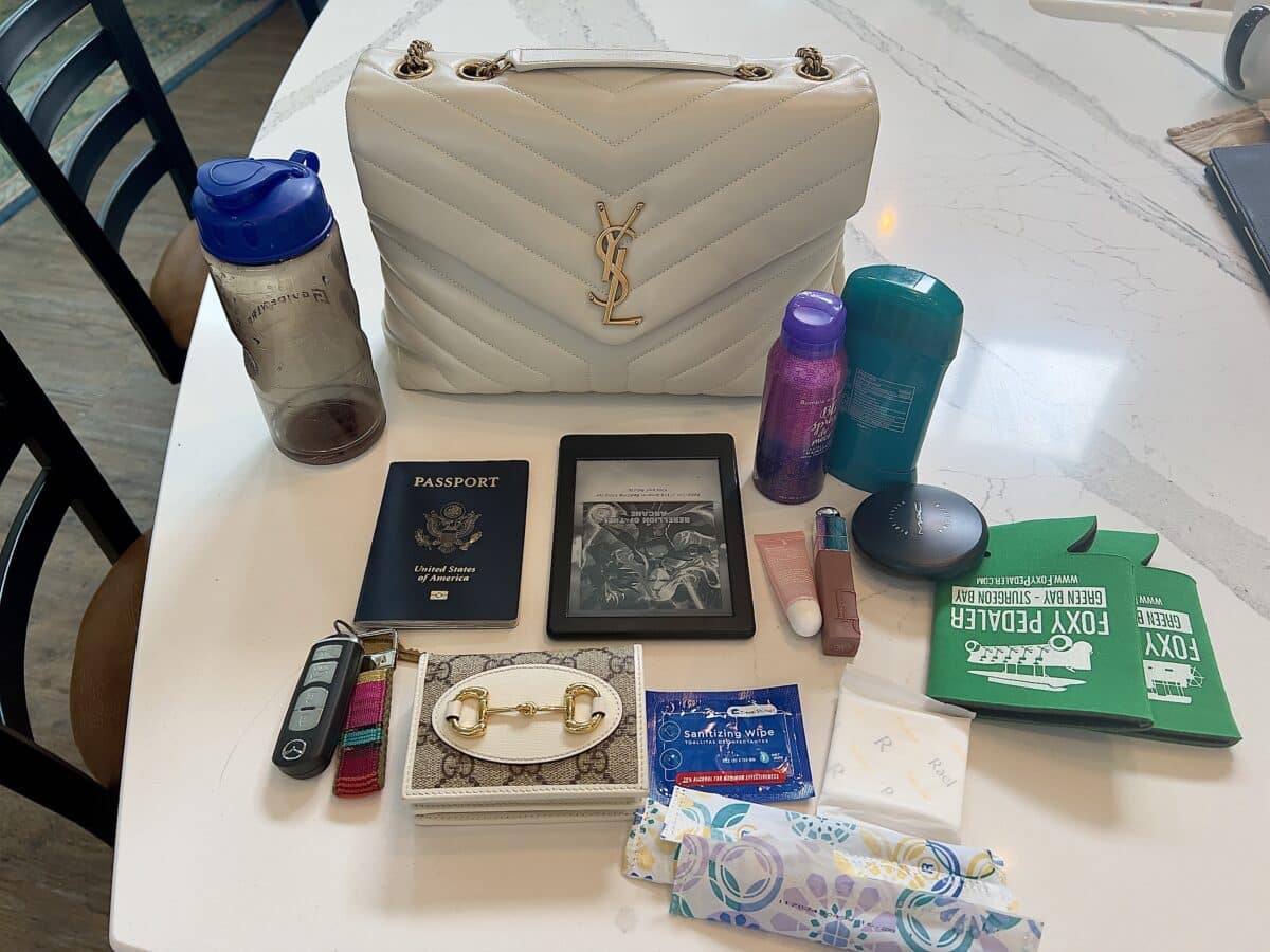 Everything I can fit in my YSL Loulou Medium featuring a water bottle, small hairspray, deodorant, tampons, pads, handwipe, wallet, Kindle, Keys, Passport, koozies 