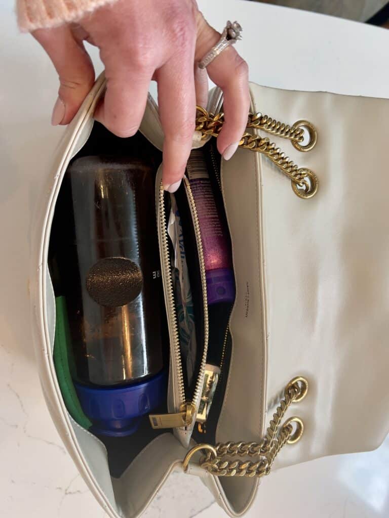 Everything I can fit in my YSL Loulou Medium featuring a water bottle, small hairspray, deodorant, tampons, pads, handwipe, wallet, Kindle, Keys, Passport, koozies