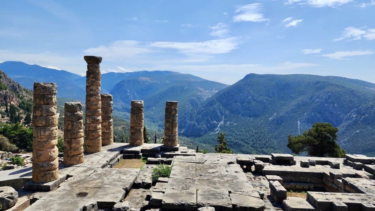 The ancient city of Delphi on a sunny day with tall stone pillars and mountains in the background