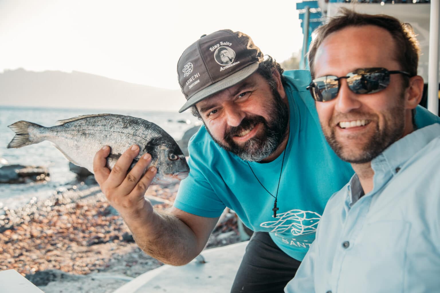 2 men smiling and wearing blue shirts while holding a fish