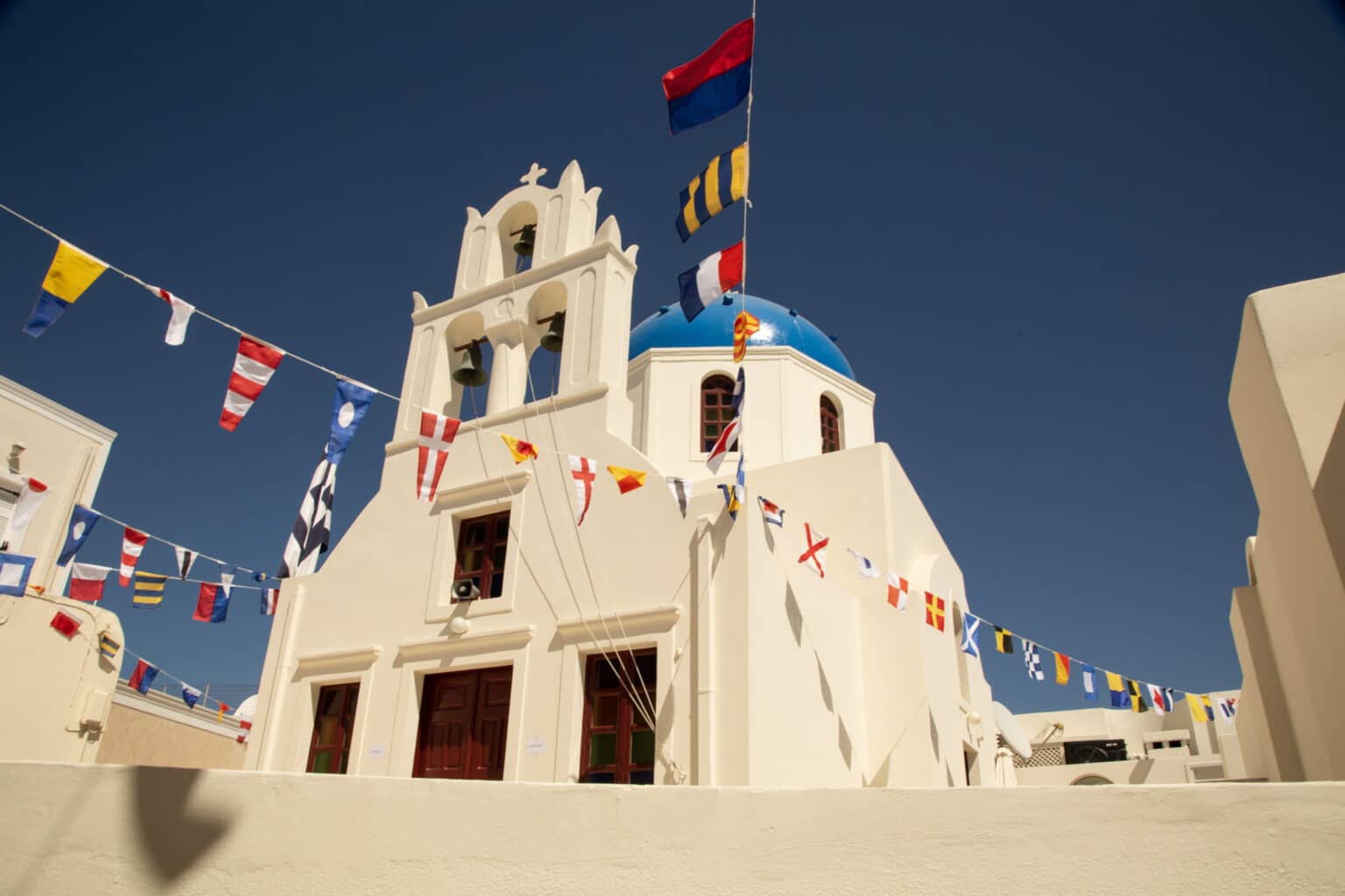 Blue dome and white church with colorful flags against a blue sky in Santorini Greece