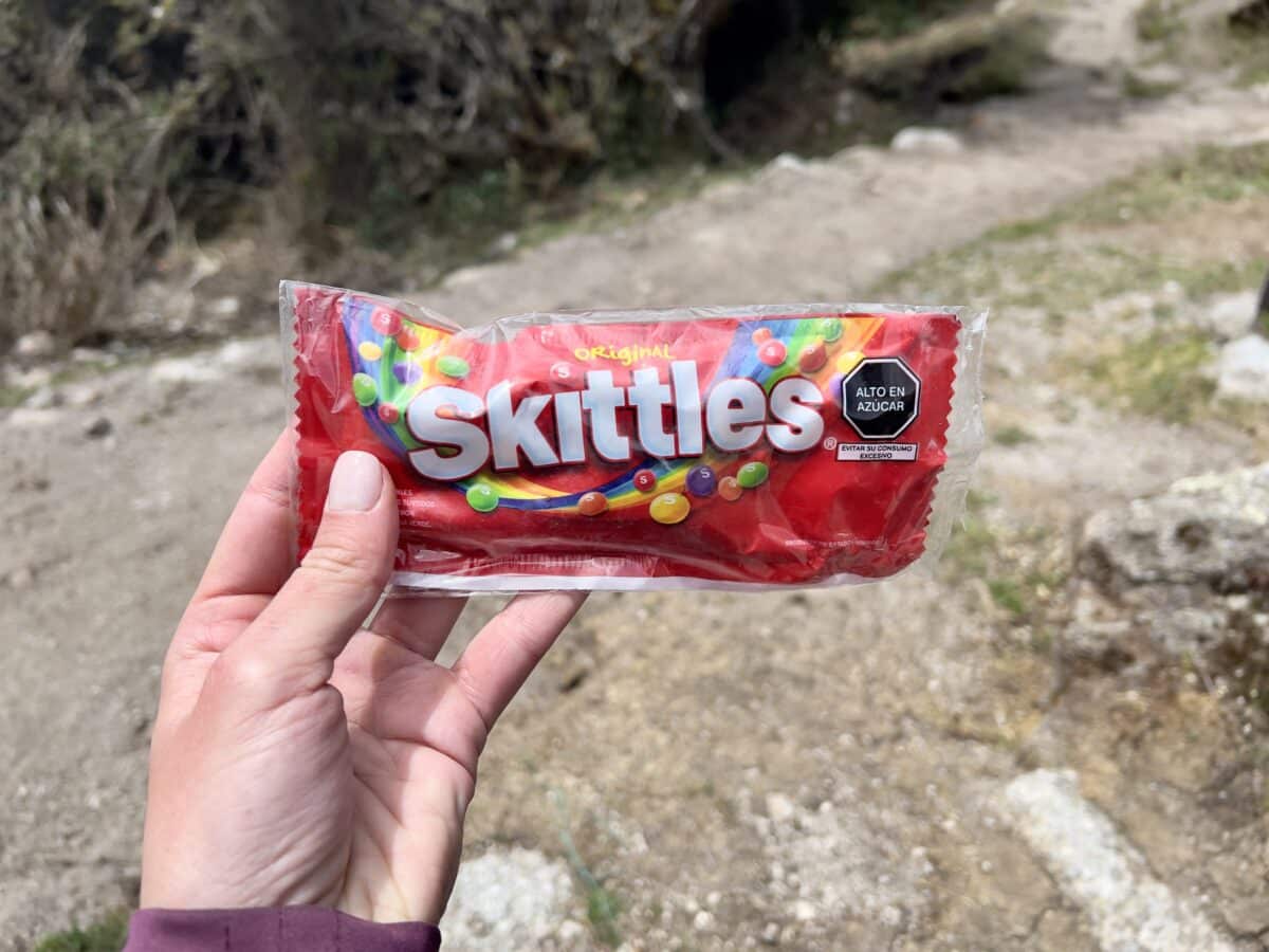 A woman holding a bag of Skittles on the Inca Trail.
