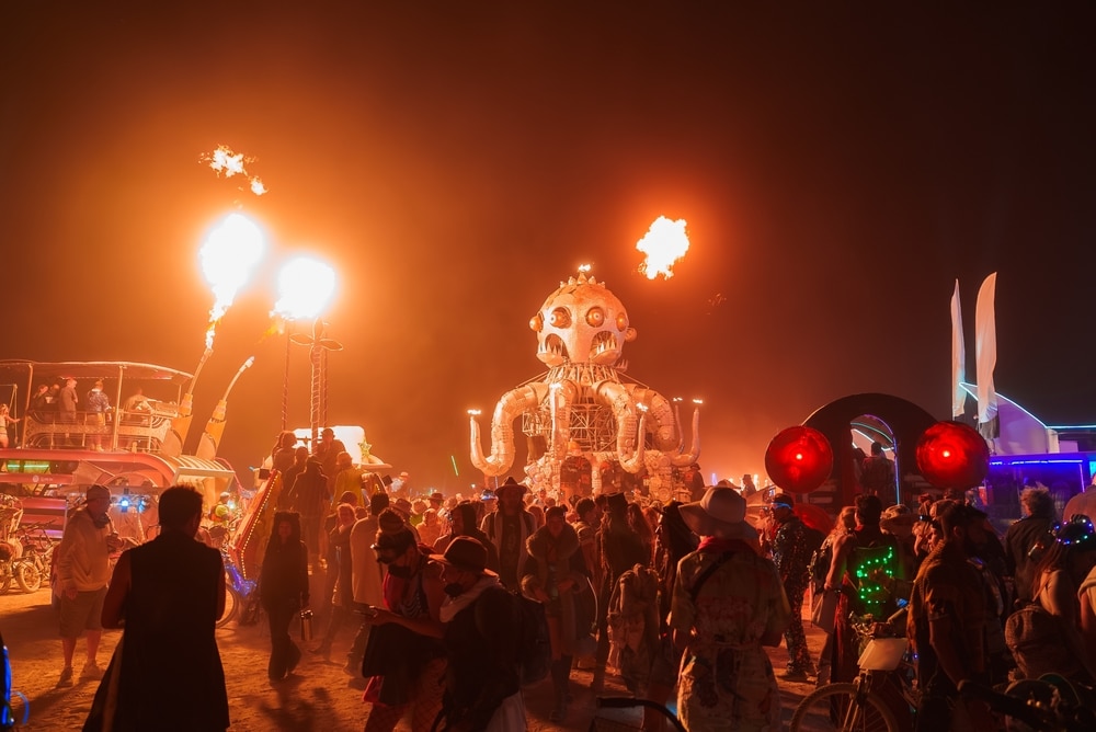 Nevada, USA. September 5, 2024. A large octopus shaped installation with fire effects captivates a crowd at Burning Man festival. Participants in colorful attire enhance the vibrant night scene.