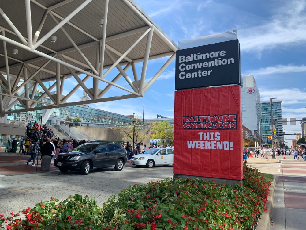 Baltimore, MD / US - October 19, 2019 - Fabric banner hung outside downtown Convention Center reads Baltimore Comic Con This Weekend at front entrance with line of millennials waiting outside