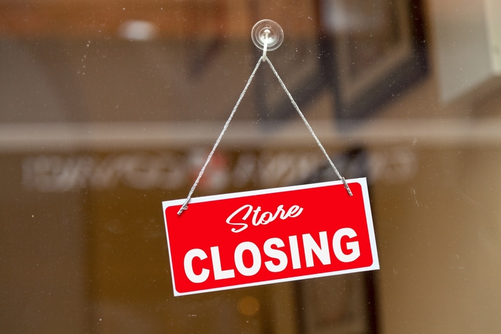 Red sign hanging at the glass door of a shop saying in English: "Store closing".