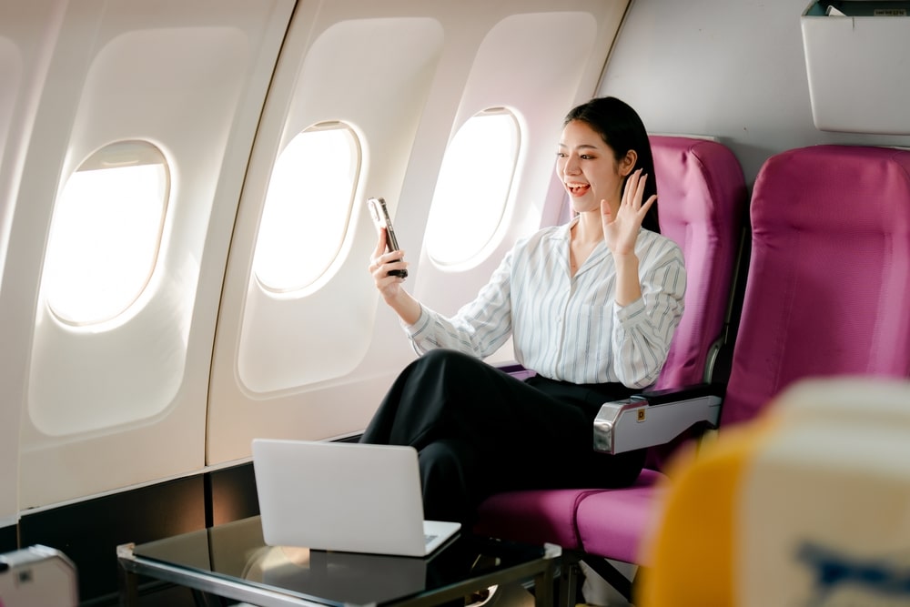 A female passenger on a plane is video calling her relatives before takeoff.