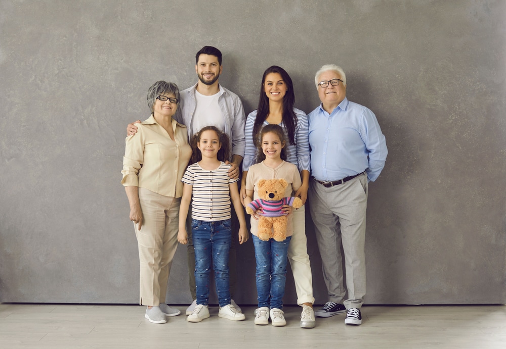 Studio photoshoot group portrait of happy big extended multi generational family. Cheerful mom, dad, grandma, grandpa and two little daughters with toy standing together, looking at camera and smiling