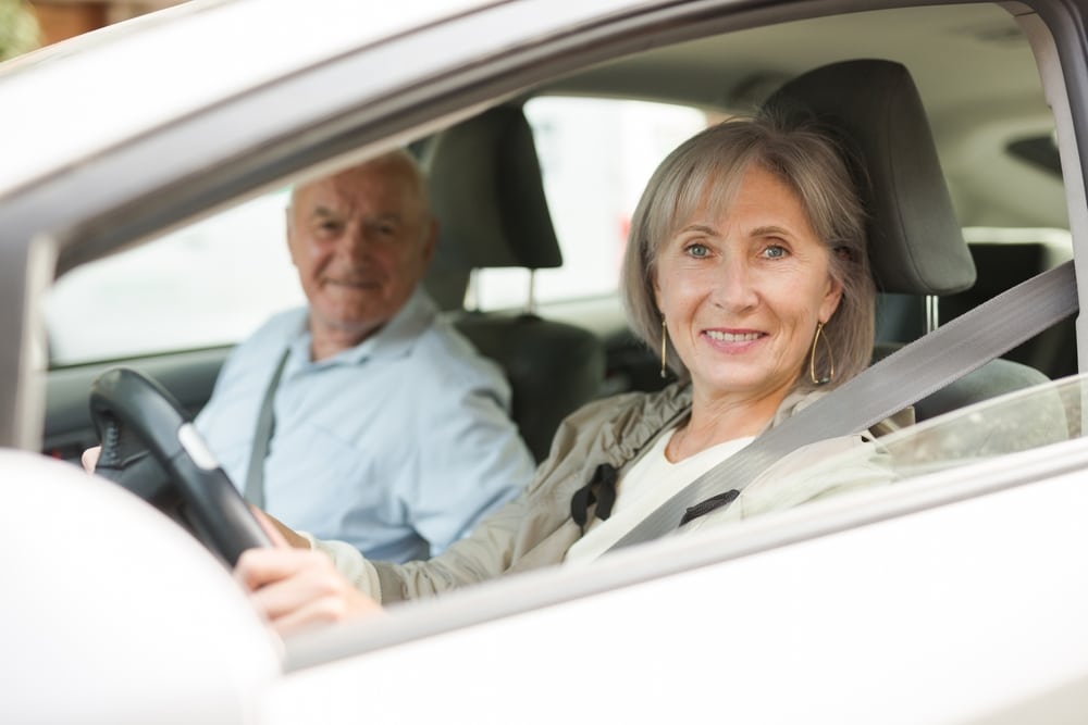 Elderly married couple driving a car in the city. Woman driving a car