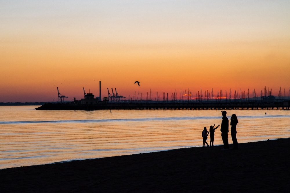 Family with two kids in silhouette watching the beautiful red, yellow sky at sunset at St Kilda Beach Melbourne, Australia