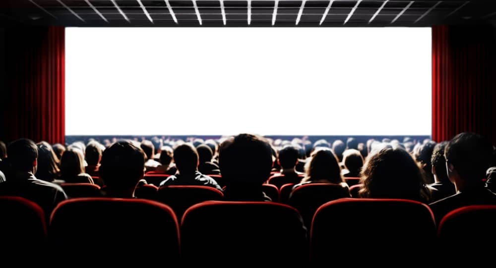 Cinema blank wide screen and people in red chairs in the cinema hall. Blurred People silhouettes watching movie performance.