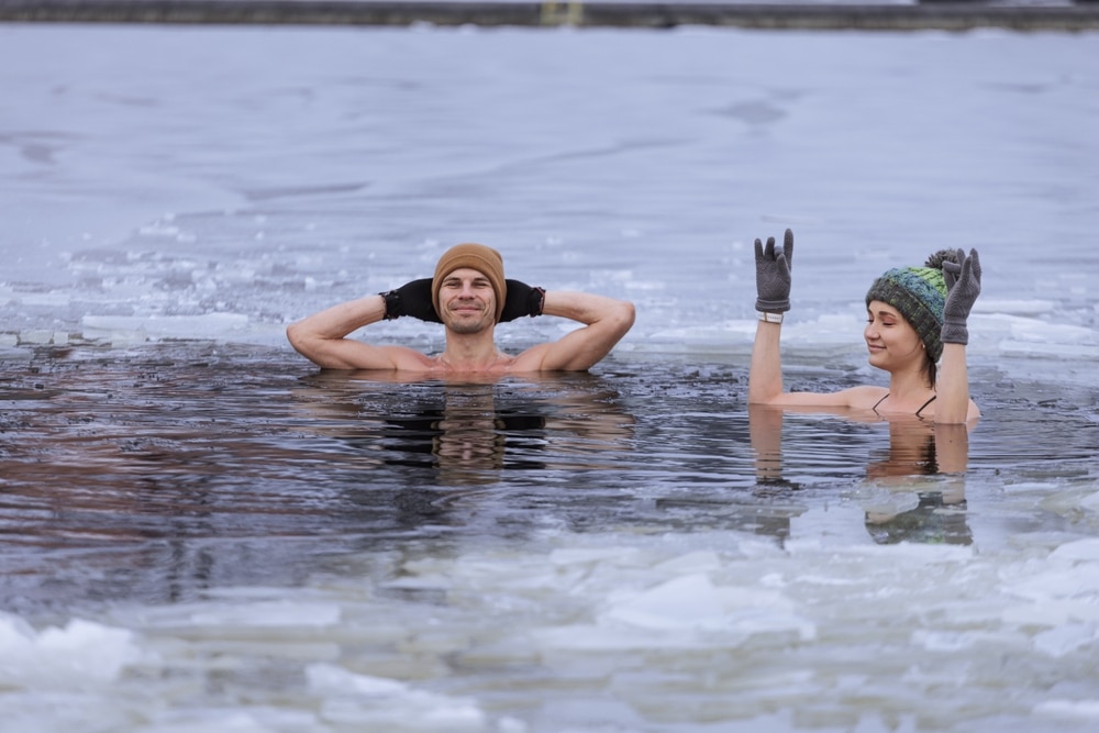 Winter swimming. Young couple ready to swim in ice water. Hat and gloves. People and nature lake in the city. Cold exposure for better health and mood. Practice to boost immunity. Nordic lifestyle