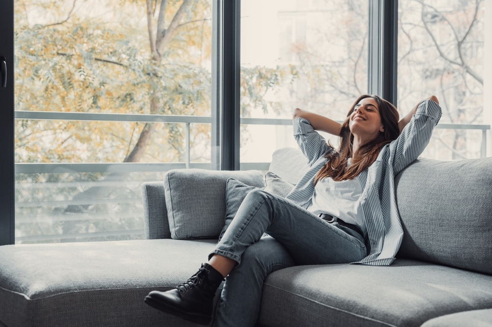 Relaxed serene pretty young woman feel fatigue lounge on comfortable sofa hands behind head rest at home, happy calm lady dream enjoy wellbeing breathing fresh air in cozy home modern living room