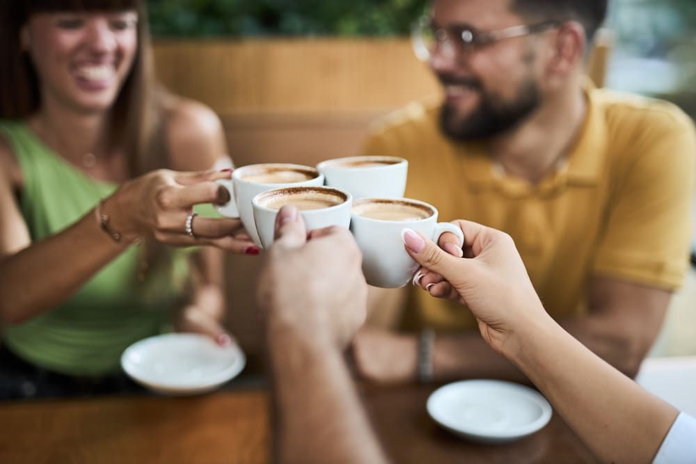 Close-up of a group of friends toasting with cups of coffee at a cafe. Focus is on cups of coffee