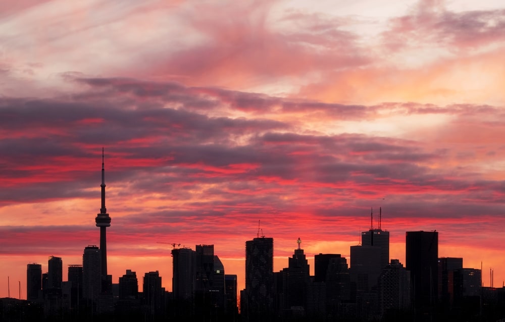 A bright pink and orange sunset with a sunpillar behind the Toronto skyline on a peaceful evening in Toronto, Ontario, Canada.