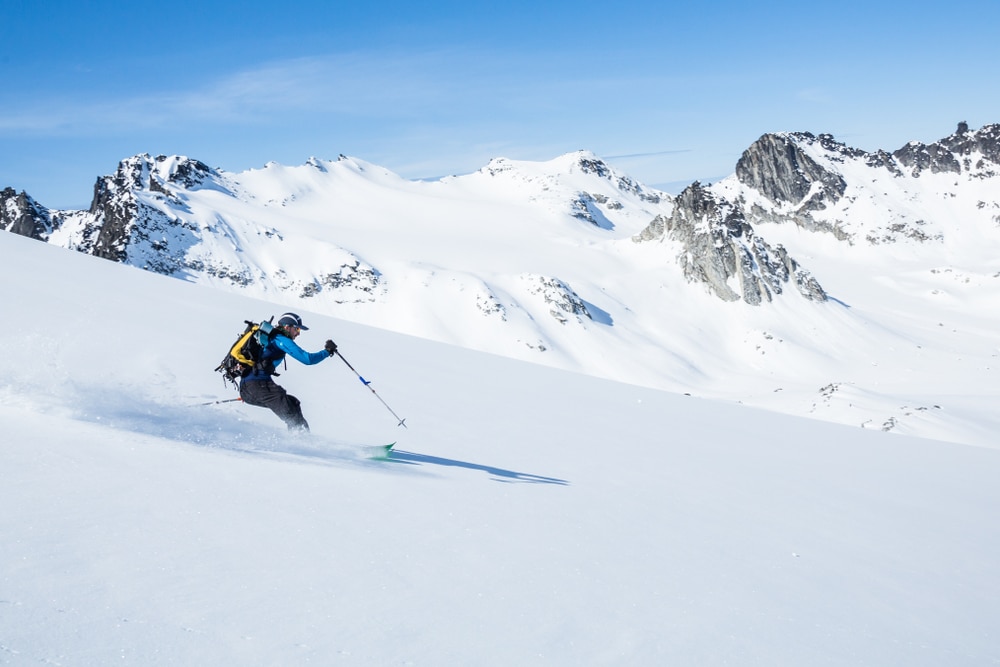 Skier on sunny day and fresh snow ripping down the slope above the Snowbird Glacier in Hatcher Pass, Alaska.