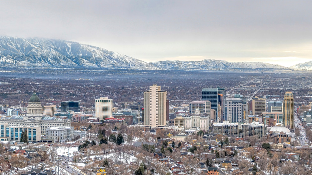 Pano Panorama of Salt Lake City with snowy mountain and gray cloudy sky in winter. Scenic aerial view of the populous downtown with nature scenery.