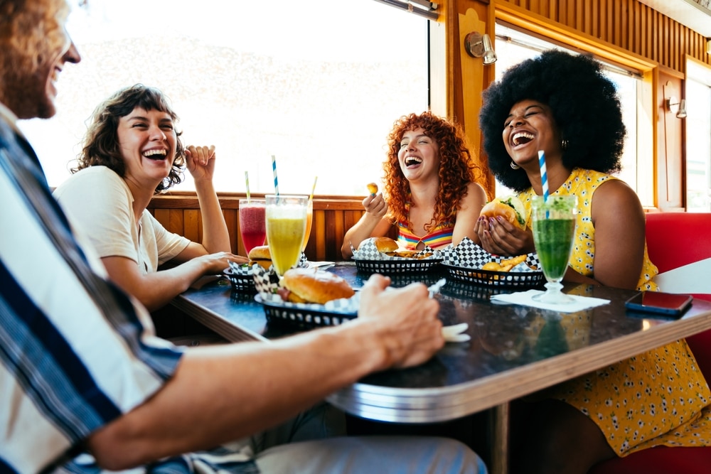 Multiethnic group of friends having meal at 80s vintage diner restaurant - Multiracial young people bonding and having fun, eating in an american fast food burger house