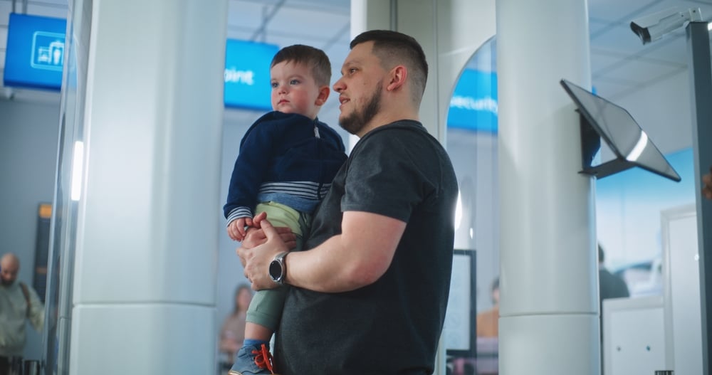 TSA Security Line in Airport: Family with Children Walking Through Metal Detector Scanner Gates. Security Officer Controls Passengers Screening Procedure for Flight Boarding, Uses Tablet Computer.