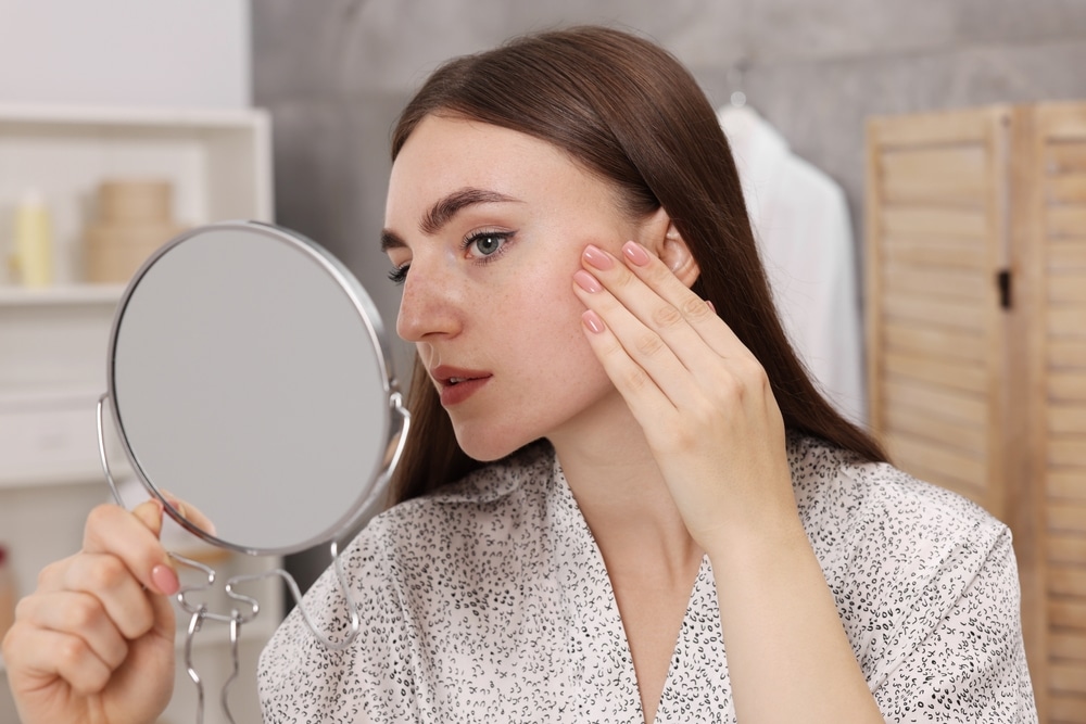 Young woman carefully looks in the mirror.