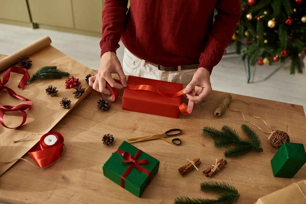 A young man meticulously wraps Christmas gifts on a table adorned with festive decorations.