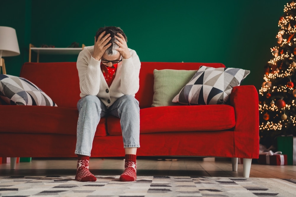Stressed senior woman sitting on a festive sofa during the holidays, thoughtful and surrounded by cozy seasonal decorations.