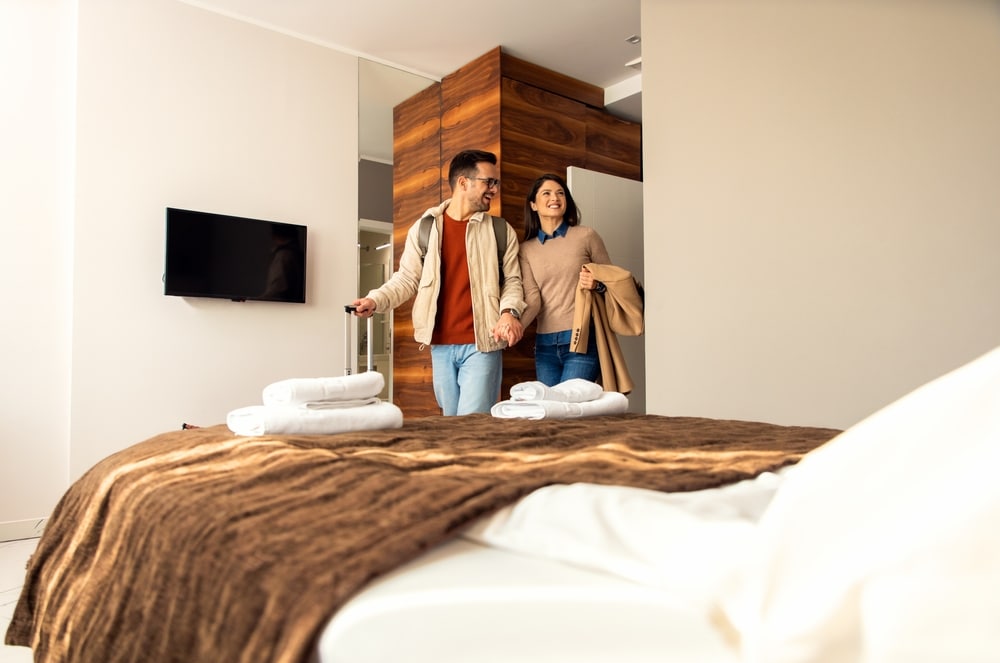 Smiling couple with suitcase arriving in hotel room.