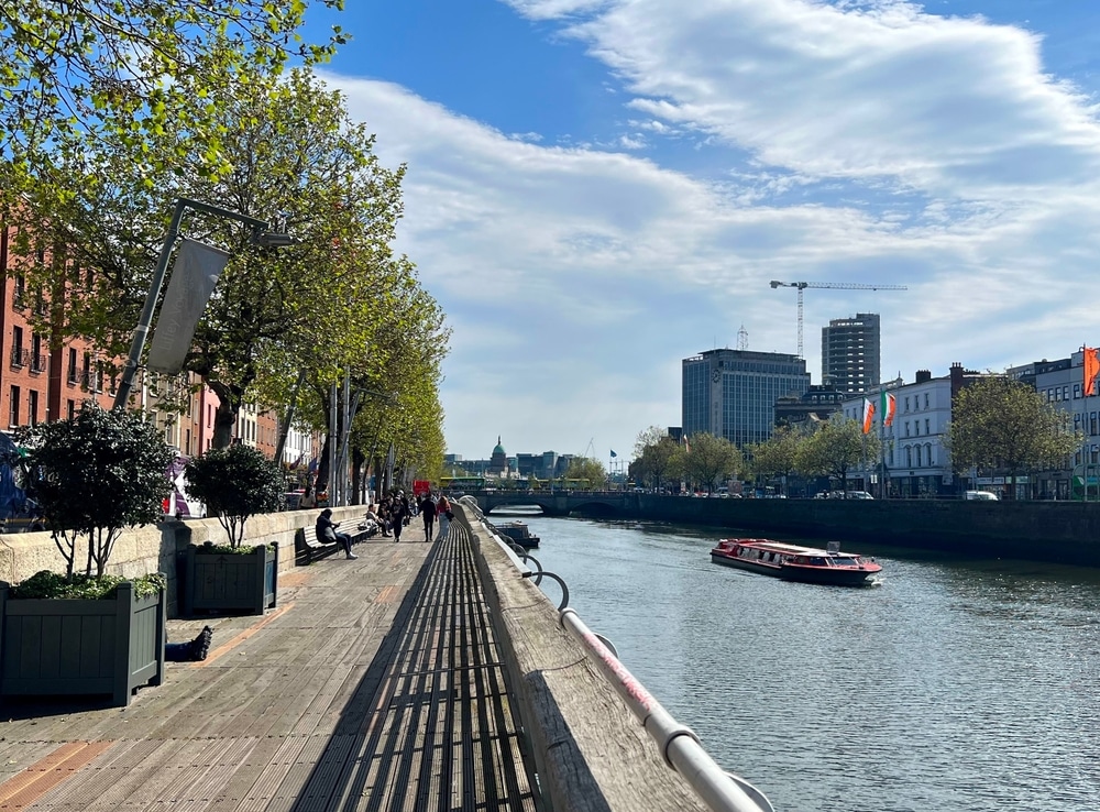 Dublin, Ireland - May 10 2024: Unidentified people walk along the River Liffey riverside boardwalk in the city center on a sunny day in Dublin, Ireland