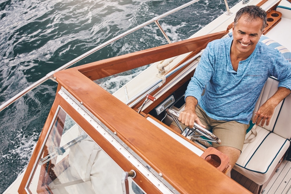 Mature man, boat and smile in water for retirement, leisure and investment for travel. Luxury, happiness and male sailor on tropical coast with adventure, yacht and transport on ocean with high angle