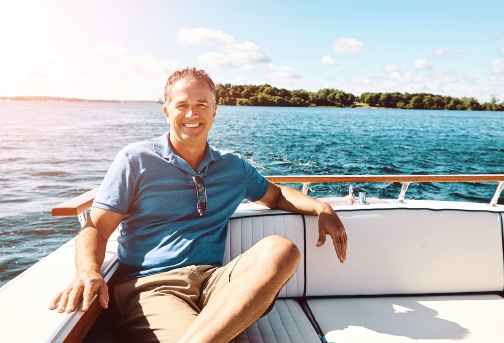 Portrait, mature man and boat on vacation for travel, sailing and adventure journey on ocean transport. Smile, male person and relax on yacht ship for holiday cruise, sea and tropical Greek island