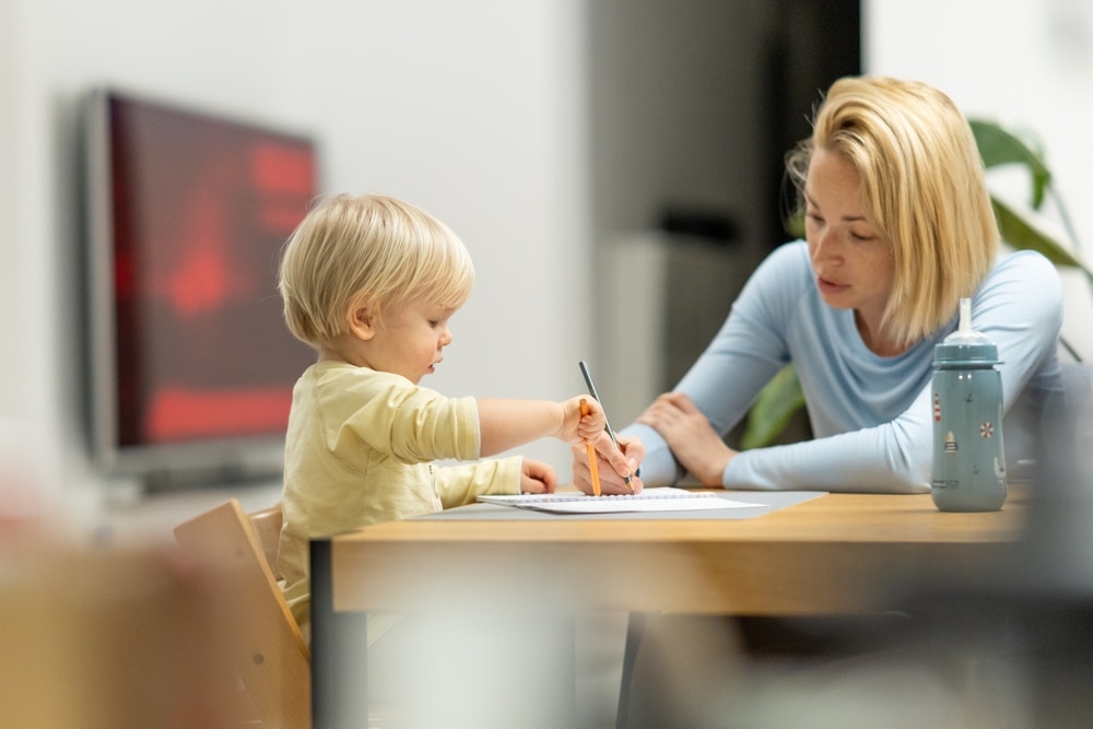 Caring young Caucasian mother and small son drawing painting in notebook at home together. Loving mom or nanny having fun learning and playing with her little 1,5 year old infant baby boy child