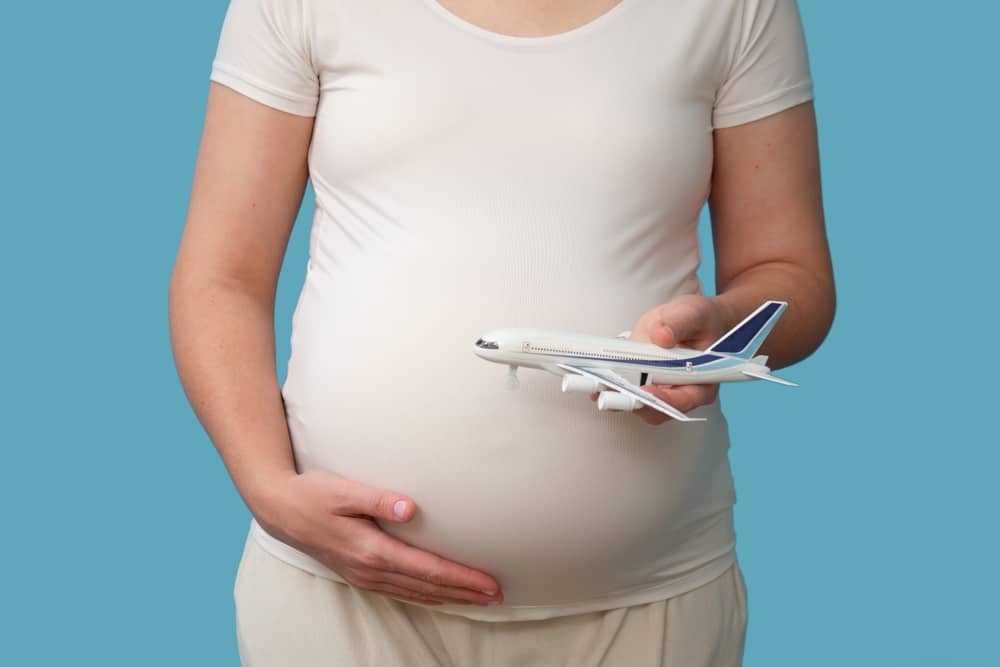 Airplane flights during pregnancy, isolated on a studio blue background. A pregnant woman holds a toy airplane, a concept