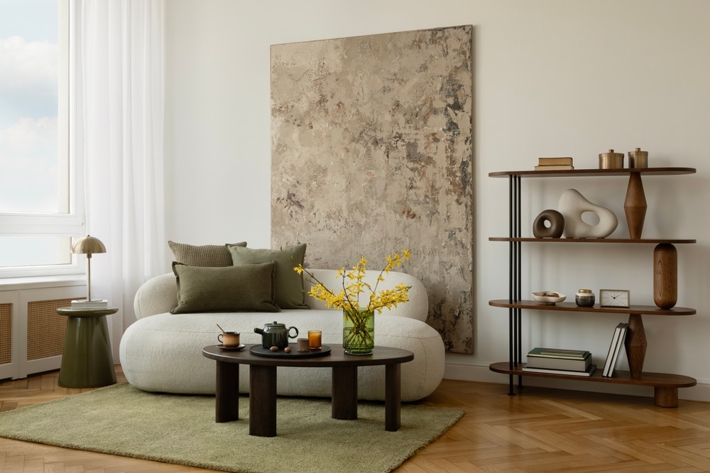 Minimalist living room with green-toned art, sculptural lamp, cozy white sofa, and a round coffee table with warm-toned decor and eucalyptus branches.