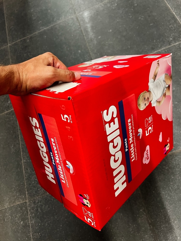 Kyiv, Ukraine - November 10, 2025: A hand grips a red Huggies diaper box, showcasing baby care product packaging and packaging design.