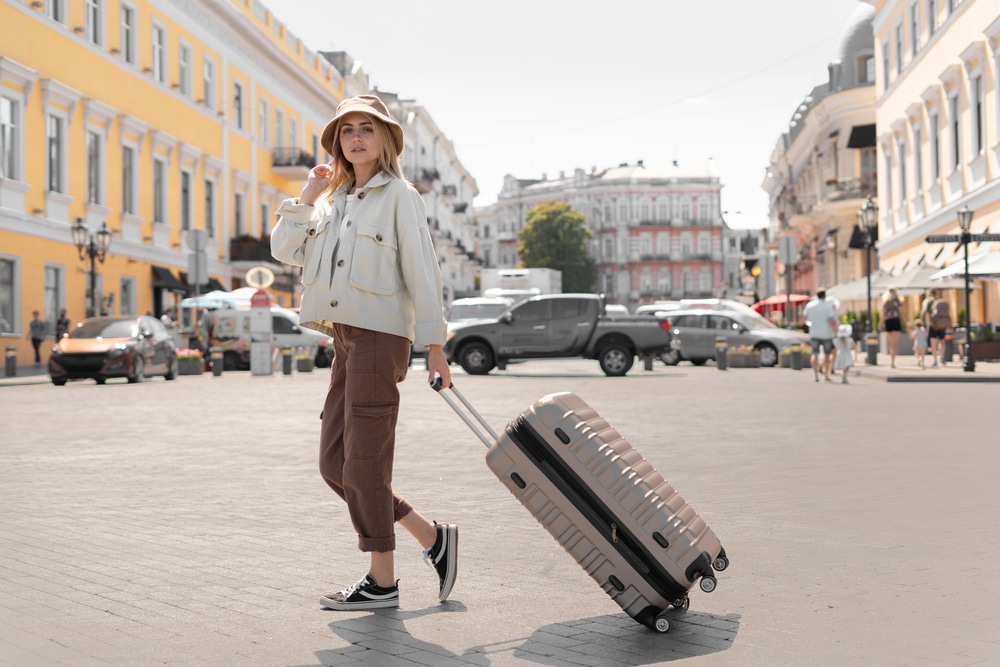 tourist woman on the street in a European city, tourism in Europe. Urban clothing style. She pulls a large suitcase with her on wheels.