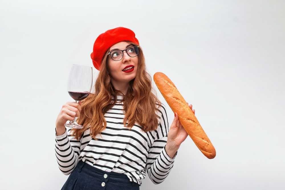 Portrait of a cheerful woman wearing beret, holding baguette and a glass of red wine