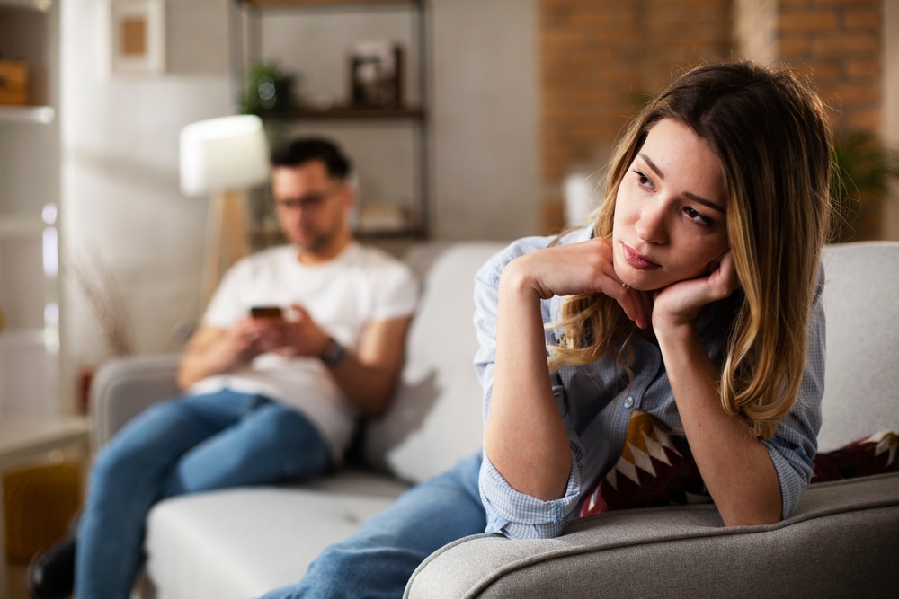 Couple at home after having a fight. Sad depressed woman sitting on sofa
