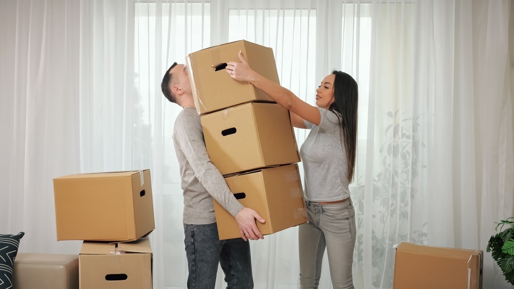 Woman helps husband carry packages in new apartment. Brown-haired wife gives man boxes and controls process of moving into purchased house