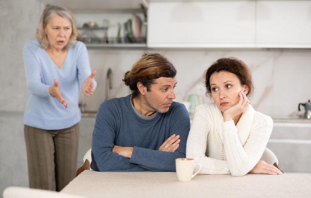 Elderly woman swears at adult children. Man and woman are sitting at table and listening to their mothers abuse