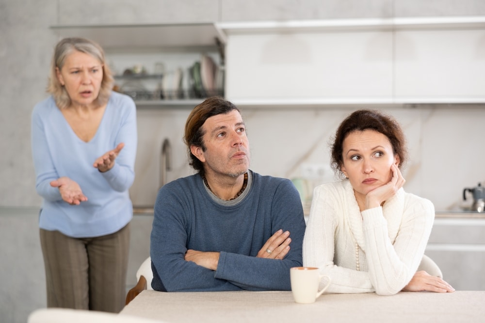 Elderly woman swears at adult children. Man and woman are sitting at table and listening to their mothers abuse