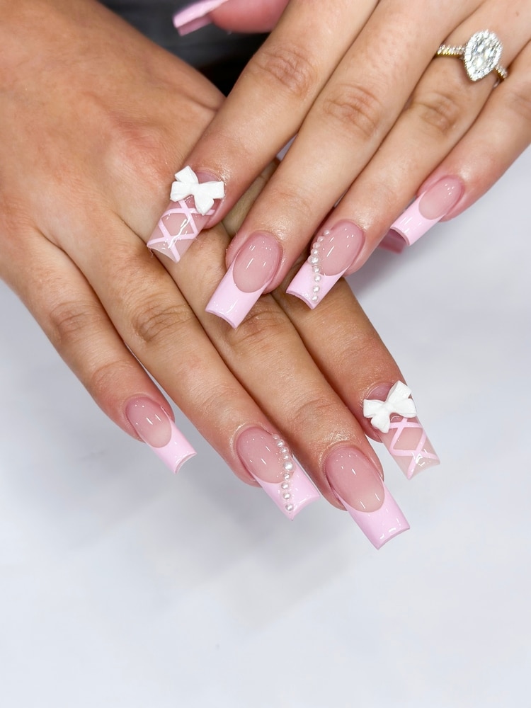 Model’s hand with pink square nails featuring cute pink bow accents, Pink Square Nails, Cute Bow Nail Art, Trendy Manicure Design. Nail salon