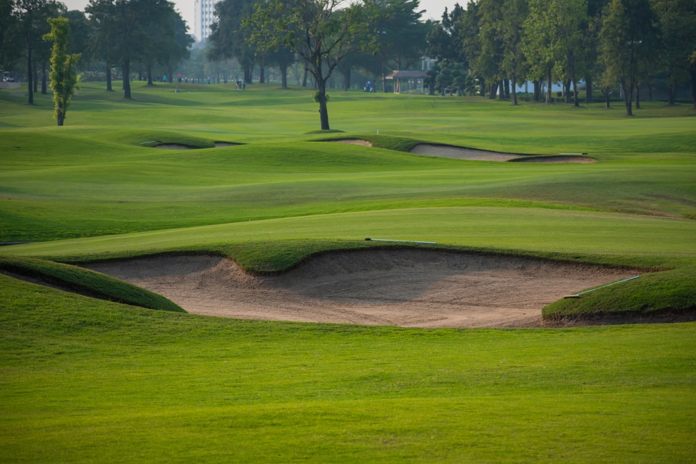 Two large sandpits occupy the forefront of a golf course landscape. Dozens of trees line the horizon with more throughout the expansive course on a sunny summer day on Mackinac Island, Michigan