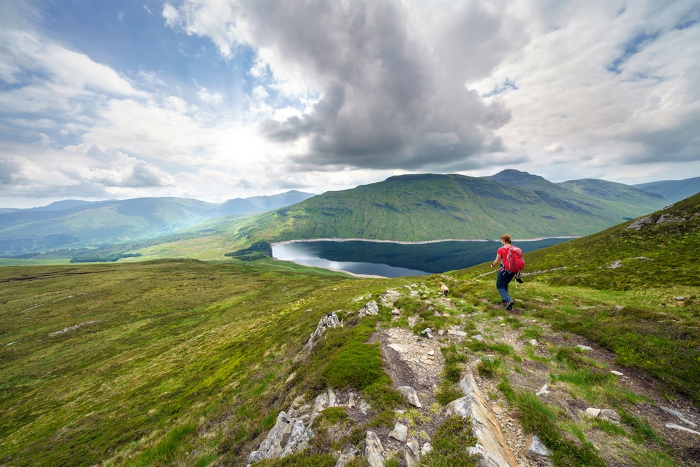 A female hiker descending the summit Meall a Phuill towards Loch an Daimh in the Scottish Highland mountains, UK landscapes.