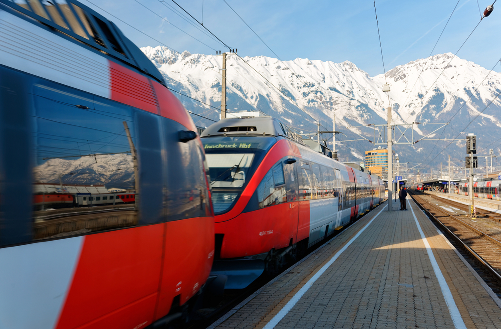 Scenery of two connected trains parking by the platform on a sunny winter day and snowy Nordkette mountains of Karwendel Alps dominating the background, at Innsbruck Main Station, Tyrol, Austria
