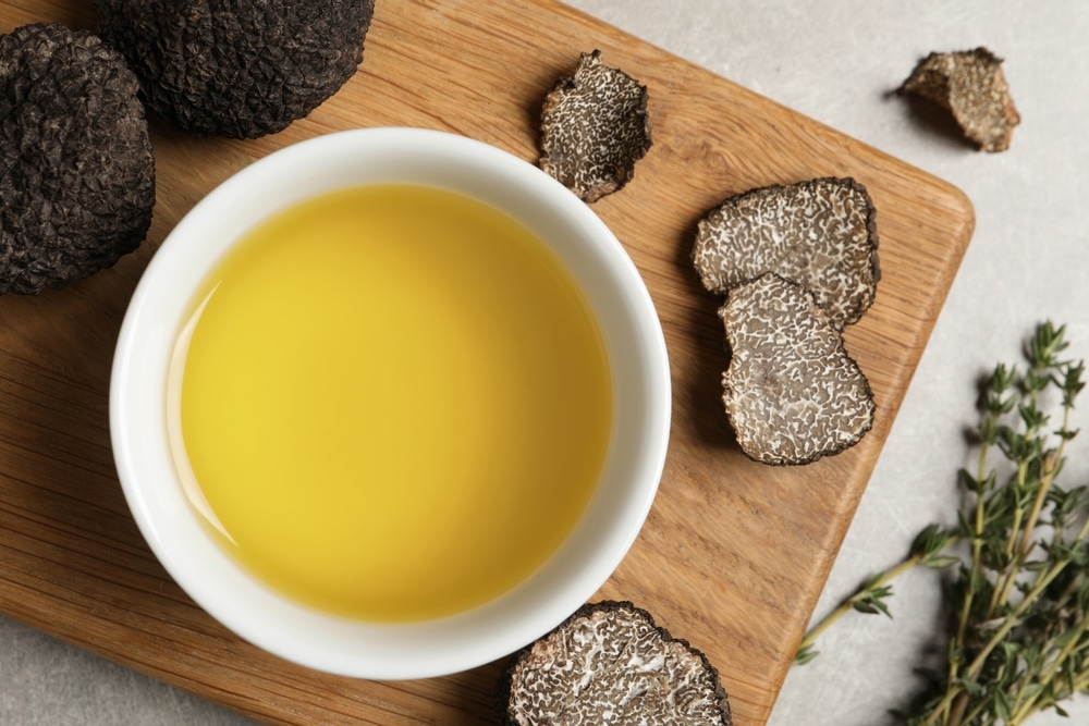 Fresh truffles, oil in bowl and thyme on light grey table, flat lay