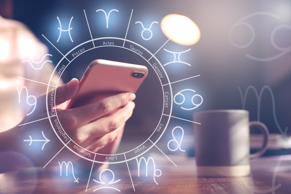 Woman with smartphone reading daily horoscope indoors, closeup
